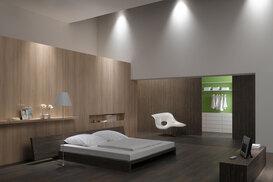 Schlafzimmerimpression von Bett, Nachtisch und Sideboard mit Holzverkleidung an Wand und indirektert Beleuchtung